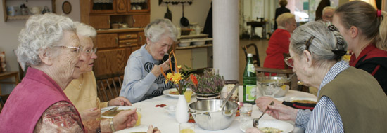 Das Foto zeigt ältere Frauen, die gemeinsam in einer Wohnküche essen.
