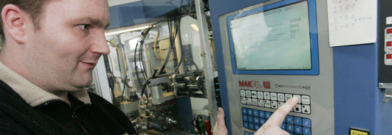 Das Foto zeigt einen jungen Mann, der das Display einer vollautomatischen Maschine bedient. Mit ihr werden Kabel auf die richtige Länge geschnitten.