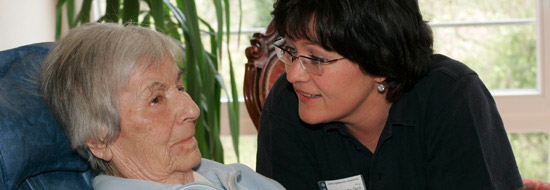 Das Foto zeigt eine Betreuerin, die sich um eine alte Frau kümmert.