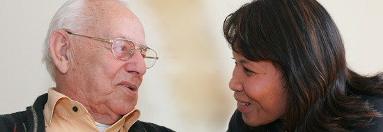 Auf dem Bild sieht man ein Gespräch zwischen einer Mitarbeiterin und einem älteren Bewohner.